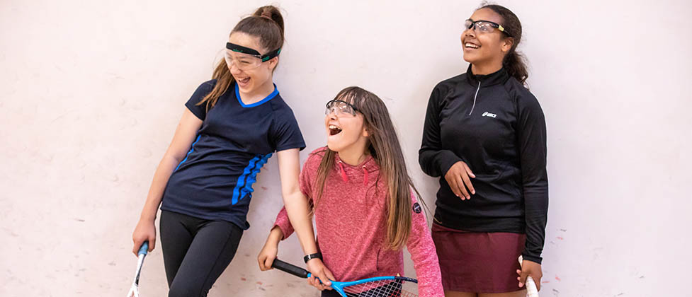 Three girls laughing on a squash court
